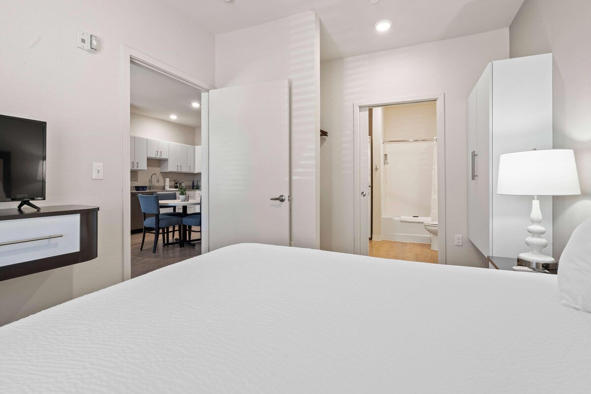 Une chambre d’hôtel comprenant un lit, un bureau, une chaise, une télévision, une salle de bain et un coin cuisine.
