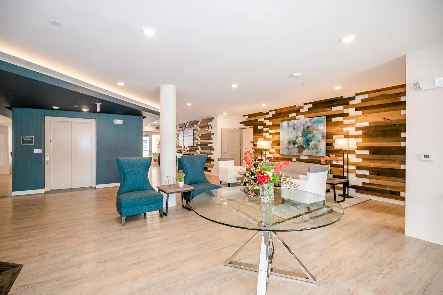 A modern lobby with teal armchairs, a glass coffee table, and a wooden accent wall.