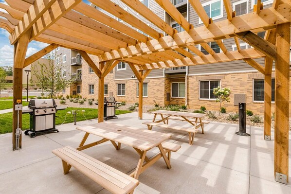 An outdoor patio area with wooden picnic tables and a grill. - Waterwalk Extended Stay Kansas City - Overland Pk (Overland Park)