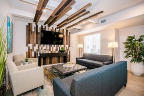 A modern living room with a flat-screen TV mounted on a wooden wall, a grey sofa, a blue sofa, and a beige armchair.