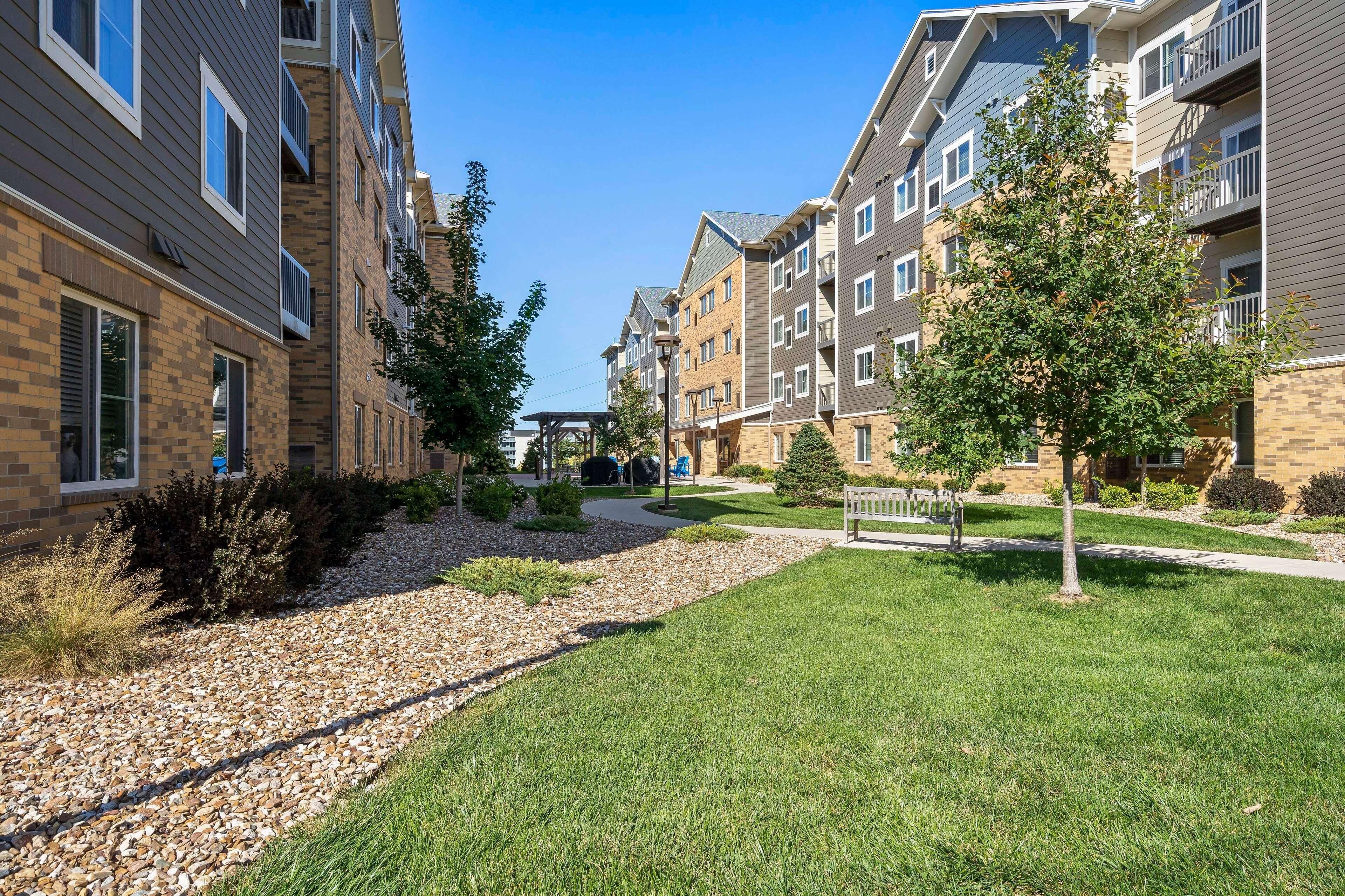 Un quartier résidentiel composé d’immeubles à plusieurs étages, d’un chemin piétonnier pavé et d’espaces verts bien entretenus.