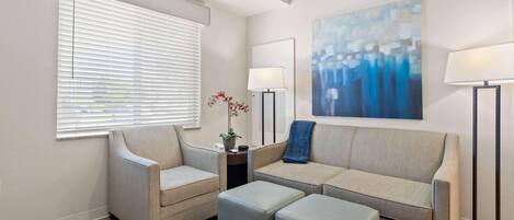 Una sala de estar con un sofá seccional, dos sillones, una mesa de centro y un tapete estampado.