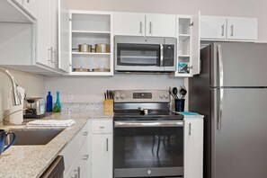 Een moderne keuken met witte kasten, een inbouwmagnetron, een roestvrijstalen oven en een koelkast.