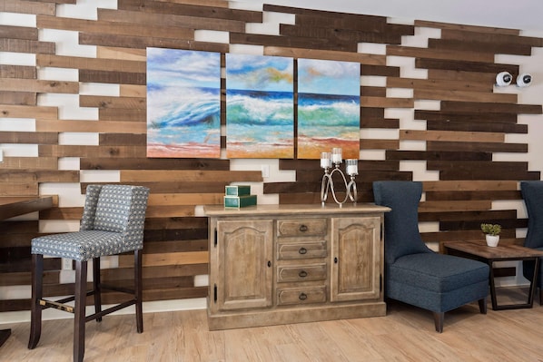 A room with a wooden wall panel, a wooden cabinet with drawers, a blue armchair, a patterned chair, and a small table with a plant. - Waterwalk Extended Stay Kansas City - Overland Pk (Overland Park)