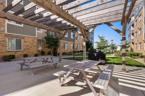 An outdoor patio area with wooden picnic tables and a barbecue grill. - Waterwalk Extended Stay Kansas City - Overland Pk (Overland Park)