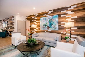Een moderne woonkamer met een grijze bank, witte fauteuils, een salontafel met een decoratief middelpunt, en een houten wand met een groot abstract schilderij.
