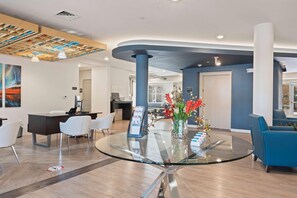 Un espace d’accueil moderne avec une table à plateau en verre, des chaises blanches et un mur d’accent bleu.