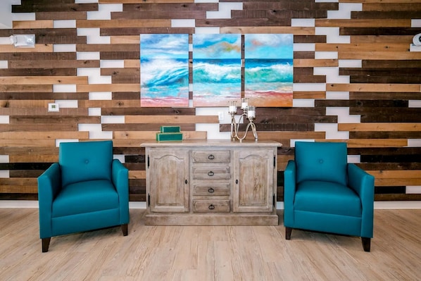 A room with a wooden wall, two teal chairs, a wooden cabinet, and a painting of a beach scene. - Waterwalk Extended Stay Kansas City - Overland Pk (Overland Park)