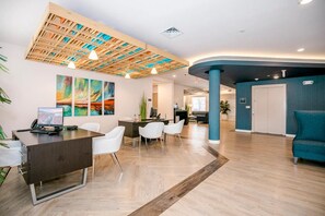 A modern reception area with a wooden ceiling, a reception desk, white chairs, and a blue accent wall. - Waterwalk Extended Stay Kansas City - Overland Pk (Overland Park)