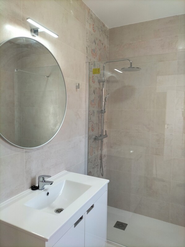 Une salle de bain avec un lavabo blanc, un miroir rond et une douche en verre avec un pommeau de douche à main.