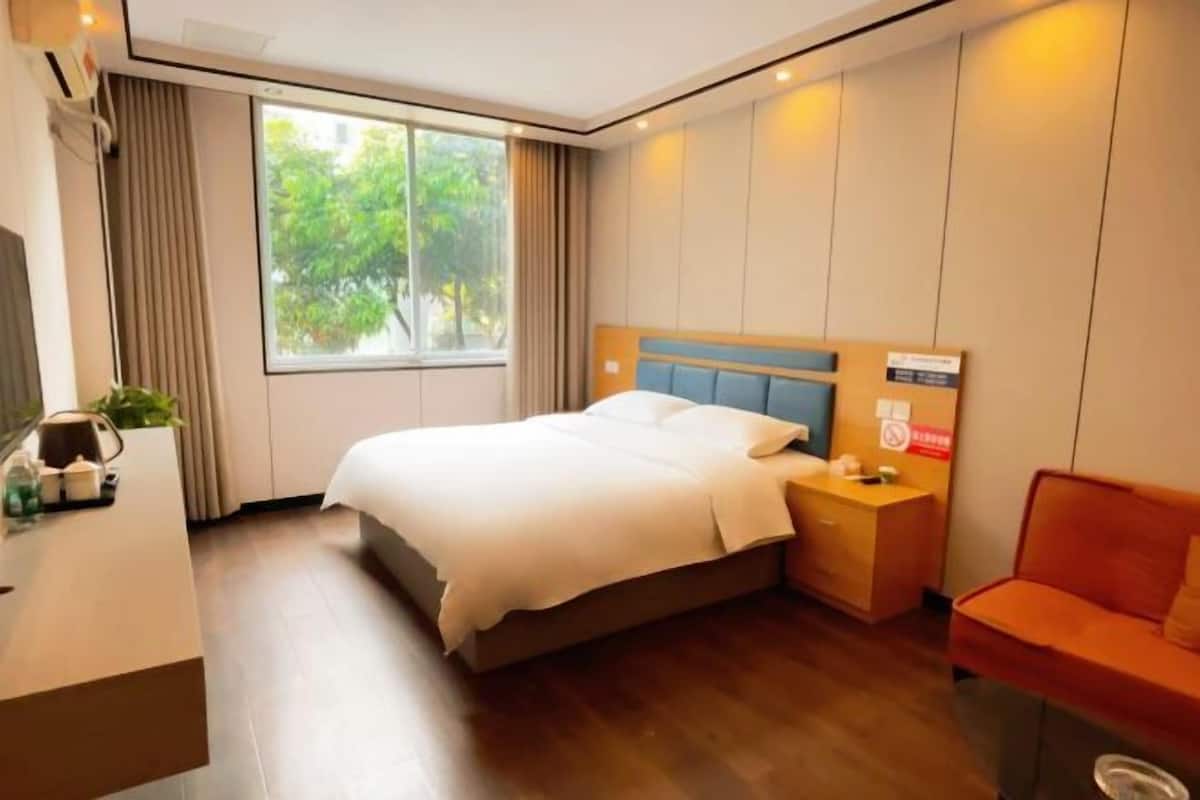 Una habitación de hotel moderna con una cama grande, una mesita de noche y un pequeño sofá naranja.
