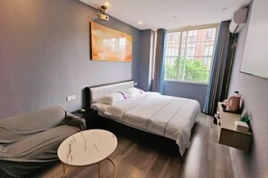 A hotel room with a bed, a round table, a painting on the wall, a window with curtains, and a small bedside table with a lamp. - Wulong Lanxin Hotel (Chongqing)