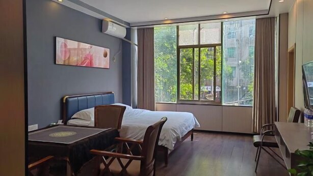 Ein Hotelzimmer mit Bett, Schreibtisch, Stuhl, Fernseher und einem Fenster mit Blick auf Grünflächen.