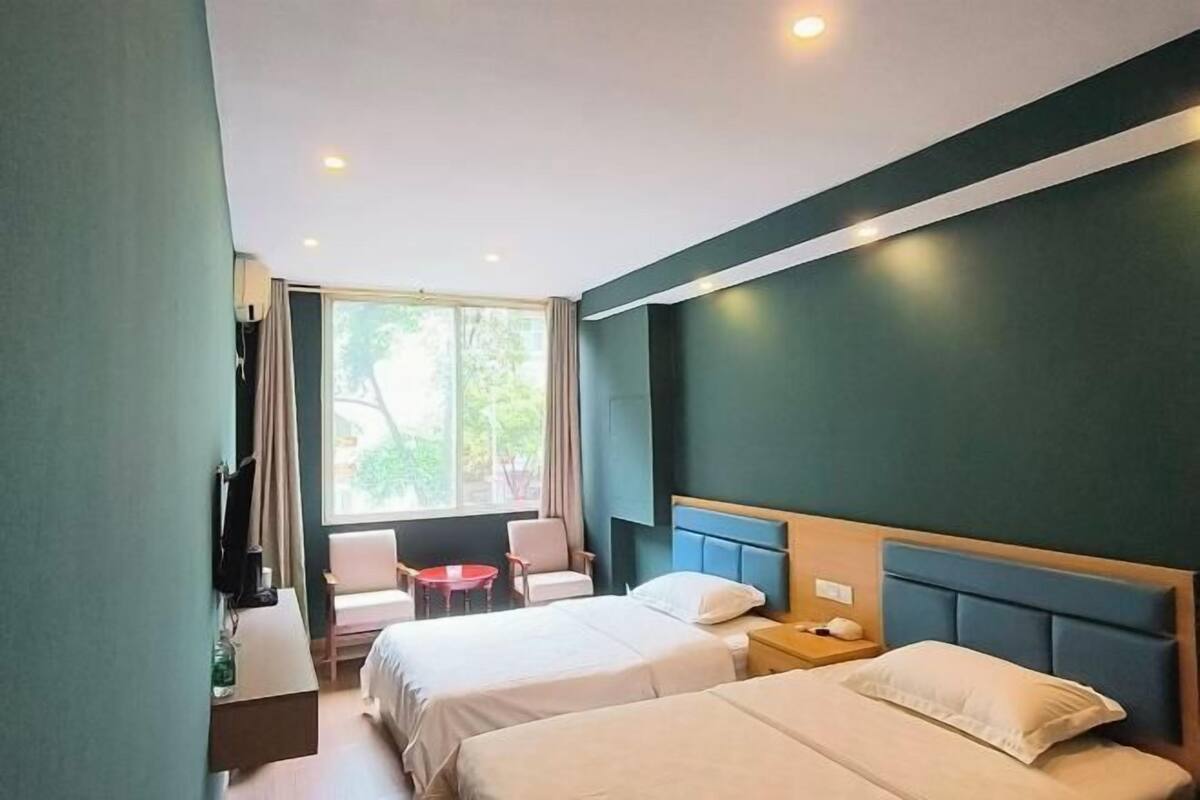 Habitación de hotel con dos camas, televisión, escritorio, silla y ventana con vista a zonas verdes.