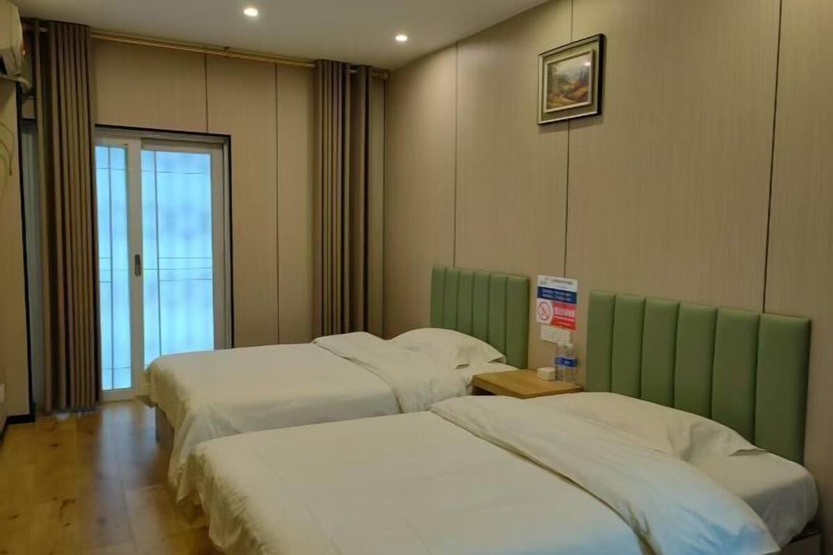 Habitación de hotel con dos camas, un cabecero verde, una ventana con cortinas y un cuadro en la pared.