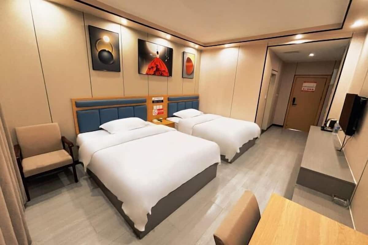 Una habitación de hotel con dos camas, un escritorio, una silla y obras de arte en las paredes.