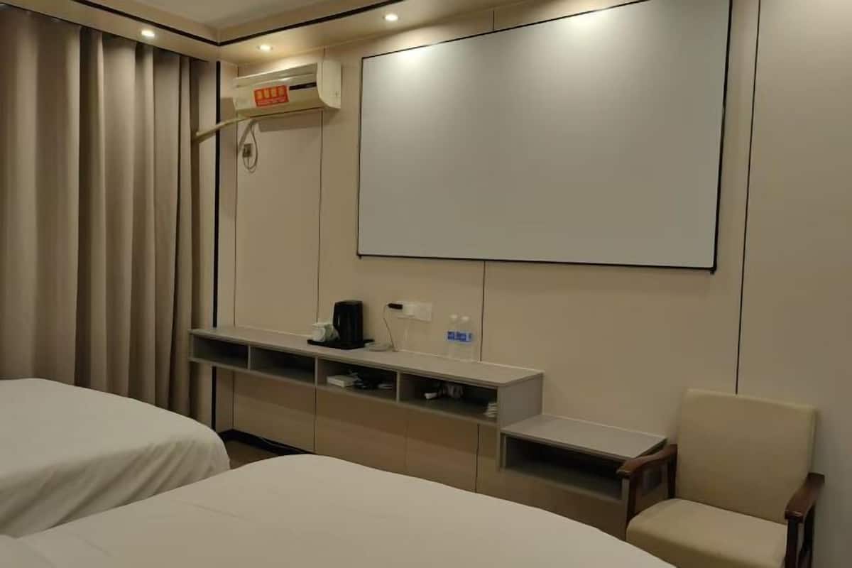 Habitación de hotel con dos camas, televisión, repisa con artículos de aseo y una silla.