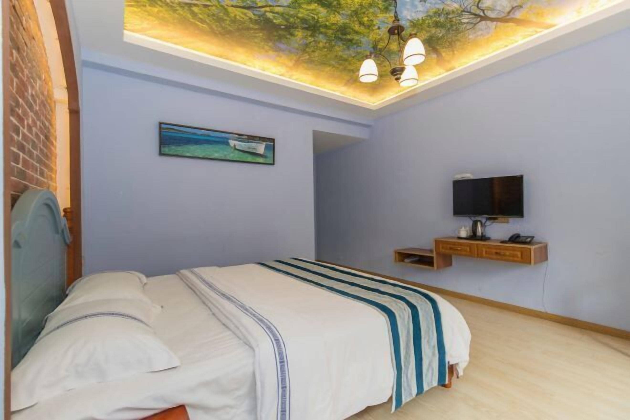 Een slaapkamer met een bed, een televisie, een muurschildering aan het plafond en een klein houten plankje.