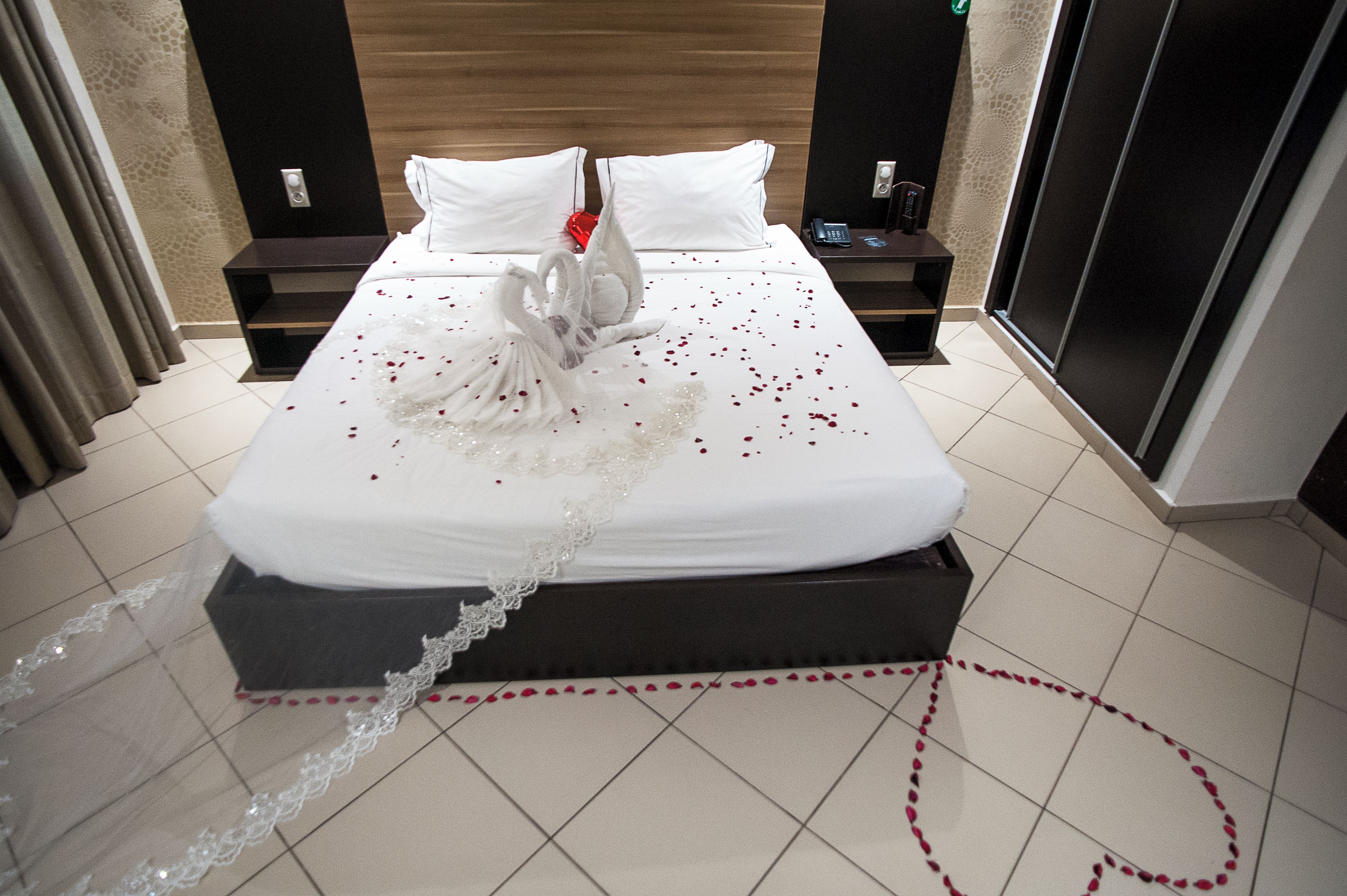 A hotel room with a neatly made bed, a decorative swan centerpiece, and a lace border on the bedspread.