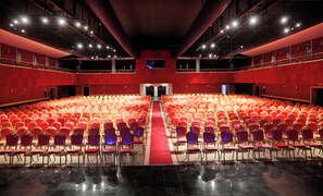 A large auditorium with rows of red and purple chairs, a central aisle, and a red carpet. - Atlantis Akbou (Béjaïa)