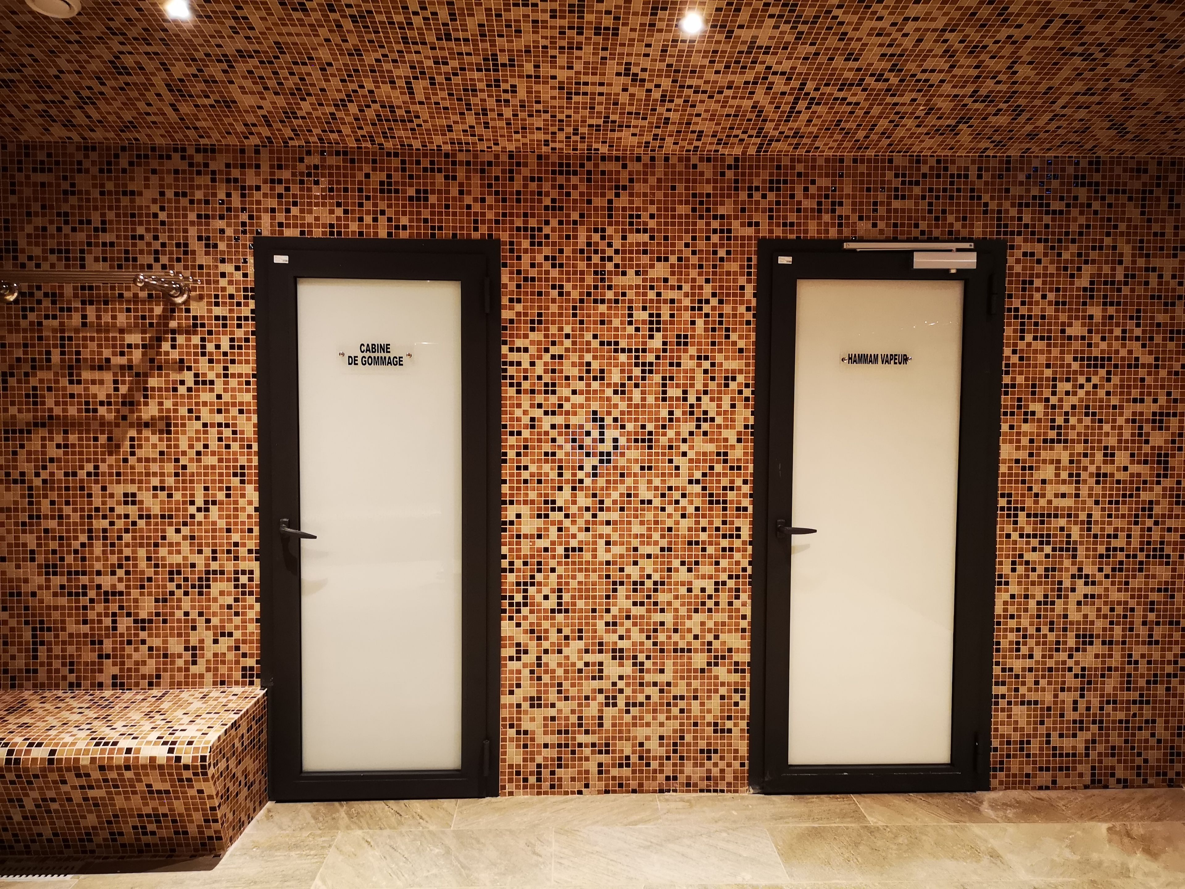 Dos puertas con los rótulos 'CABINE DE GOMMAGE' y 'HAMMAM VAUPEUR' en una habitación con paredes de azulejos.