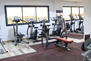 Un gimnasio con equipo de ejercicio, una banca y ventanas amplias.