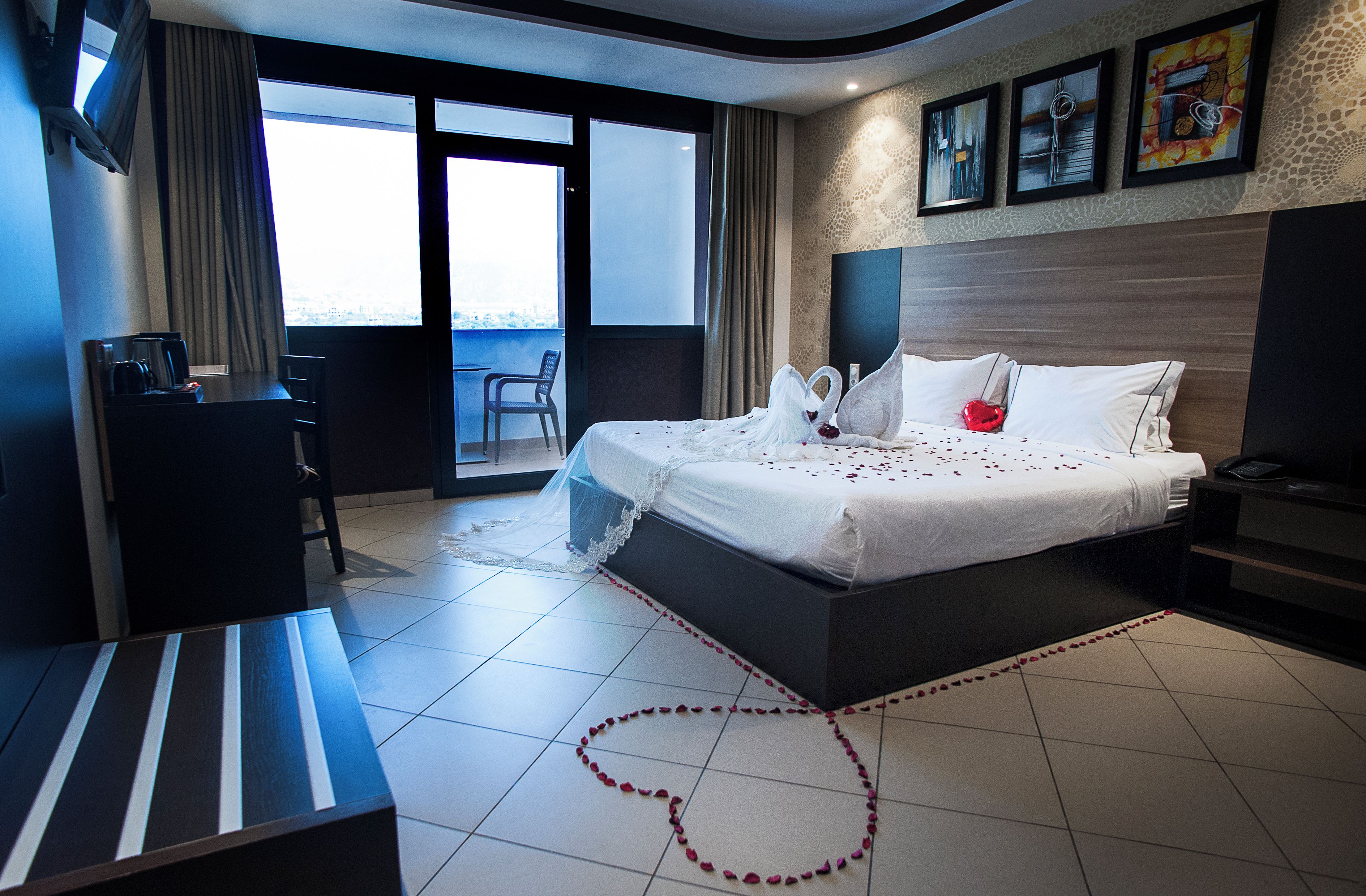 Une chambre d’hôtel avec un lit, un bureau, une chaise, un balcon et des œuvres d’art accrochées au mur.