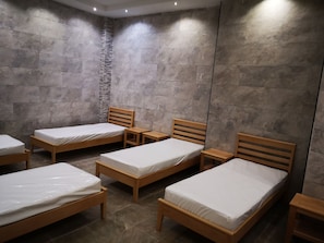 Una habitación con seis camas de madera dispuestas en dos filas, cada una con una mesita de noche de madera.