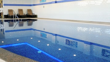 Piscina com água azul cristalina, parede azulejada e três espreguiçadeiras.