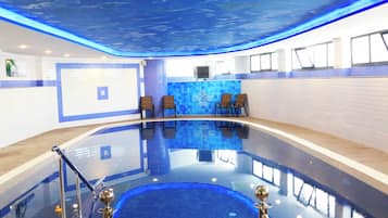 A swimming pool with a blue ceiling, lounge chairs, and a tiled wall.