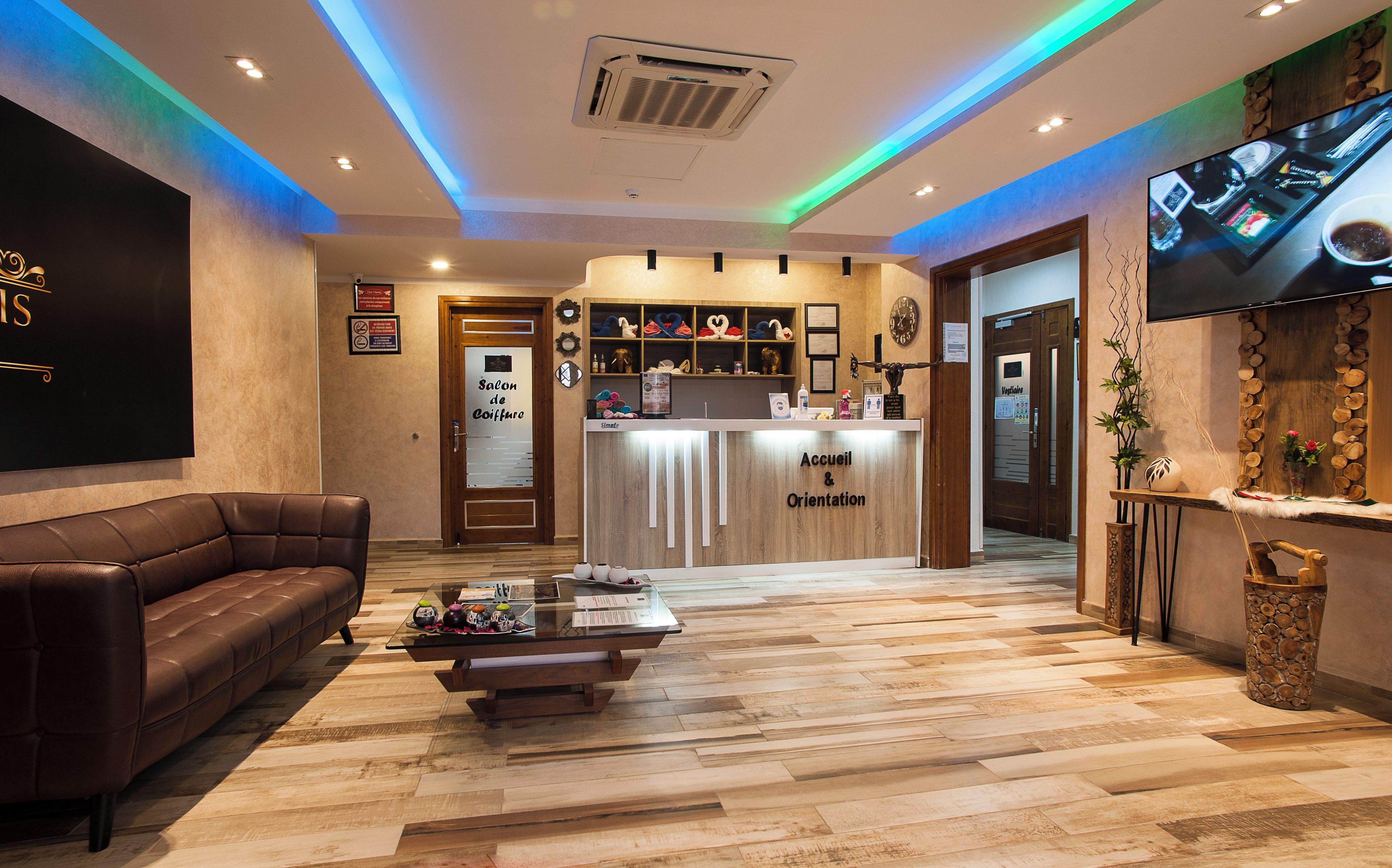 A hotel reception area with a reception desk, a brown leather sofa, a coffee table, and a television mounted on the wall.