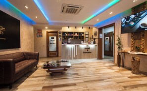 A hotel reception area with a reception desk, a brown leather sofa, a coffee table, and a television mounted on the wall.
