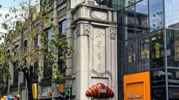 A building with classical architecture, a modern glass facade, and a storefront with a distinctive orange sign.