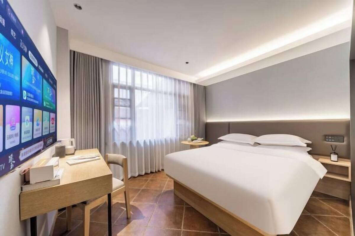 Habitación de hotel con cama, escritorio, silla, televisor y ventana con cortinas.