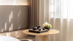 A modern room with a round wooden table, a sofa, and a window with curtains. - Xinyitian Hotel (Wenzhou Xueshan Road Wuma Street Branch) (Wenzhou)