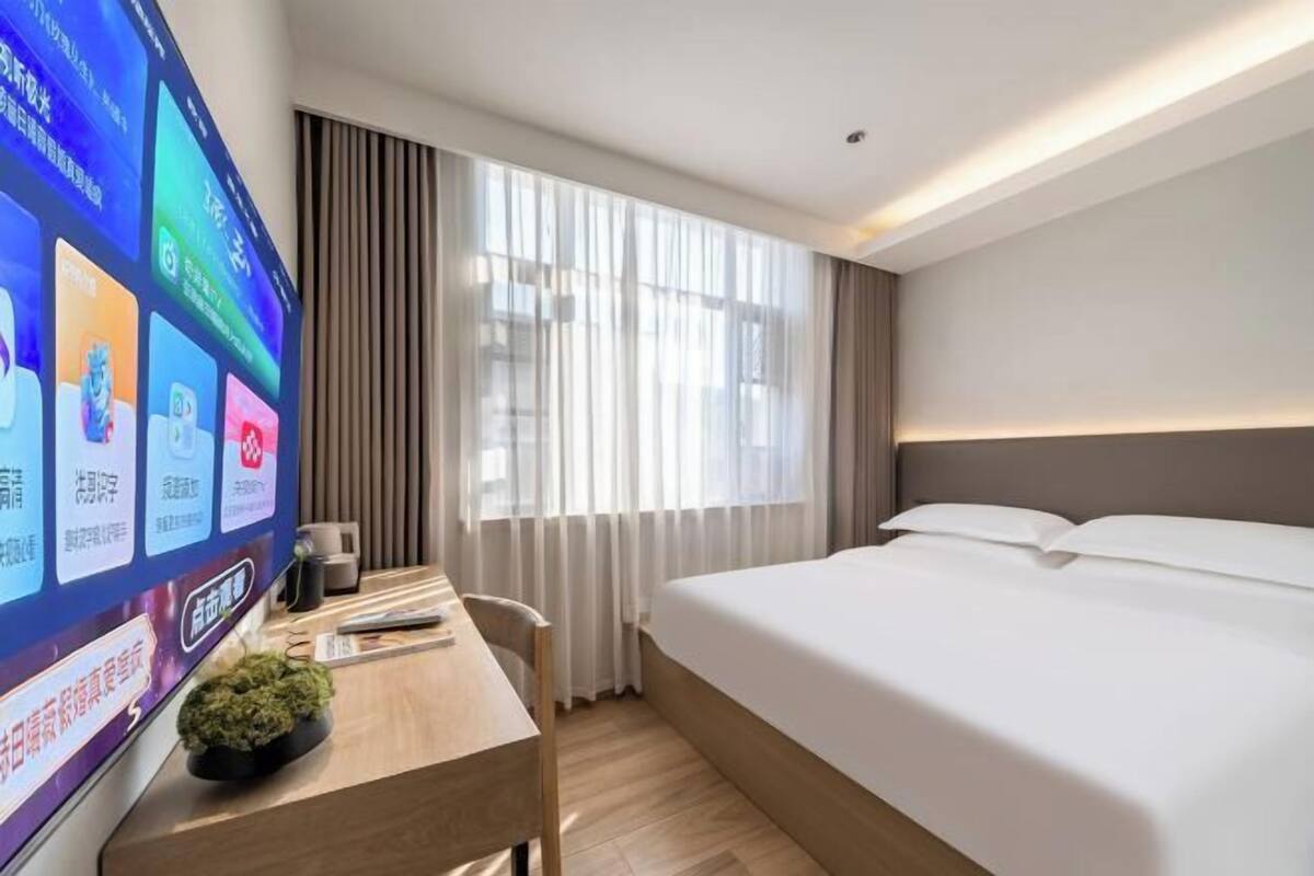 Una habitación de hotel con una cama, un escritorio con ordenador, televisión y ventana con cortinas.