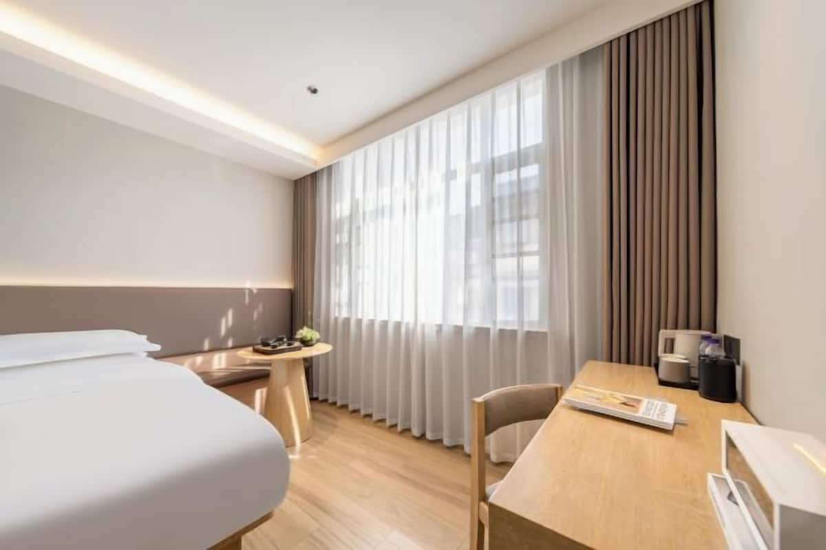 Habitación de hotel con cama, escritorio, silla, mesita y ventana con cortinas.