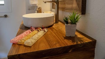 A bathroom with a wooden vanity, a white sink, and a small potted plant.