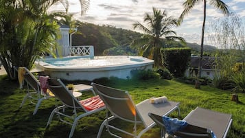 A pool area with lounge chairs and a small table, surrounded by palm trees and a grassy lawn.