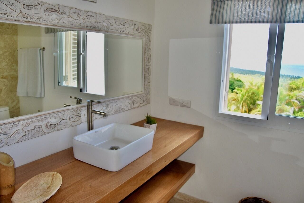 Casa de banho com toucador em madeira, lavatório branco e espelho grande com moldura decorativa.