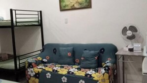 Ein Zimmer mit einem Etagenbett, einem Sofa mit floralem Bezug, einem Ventilator und einem Bild an der Wand.