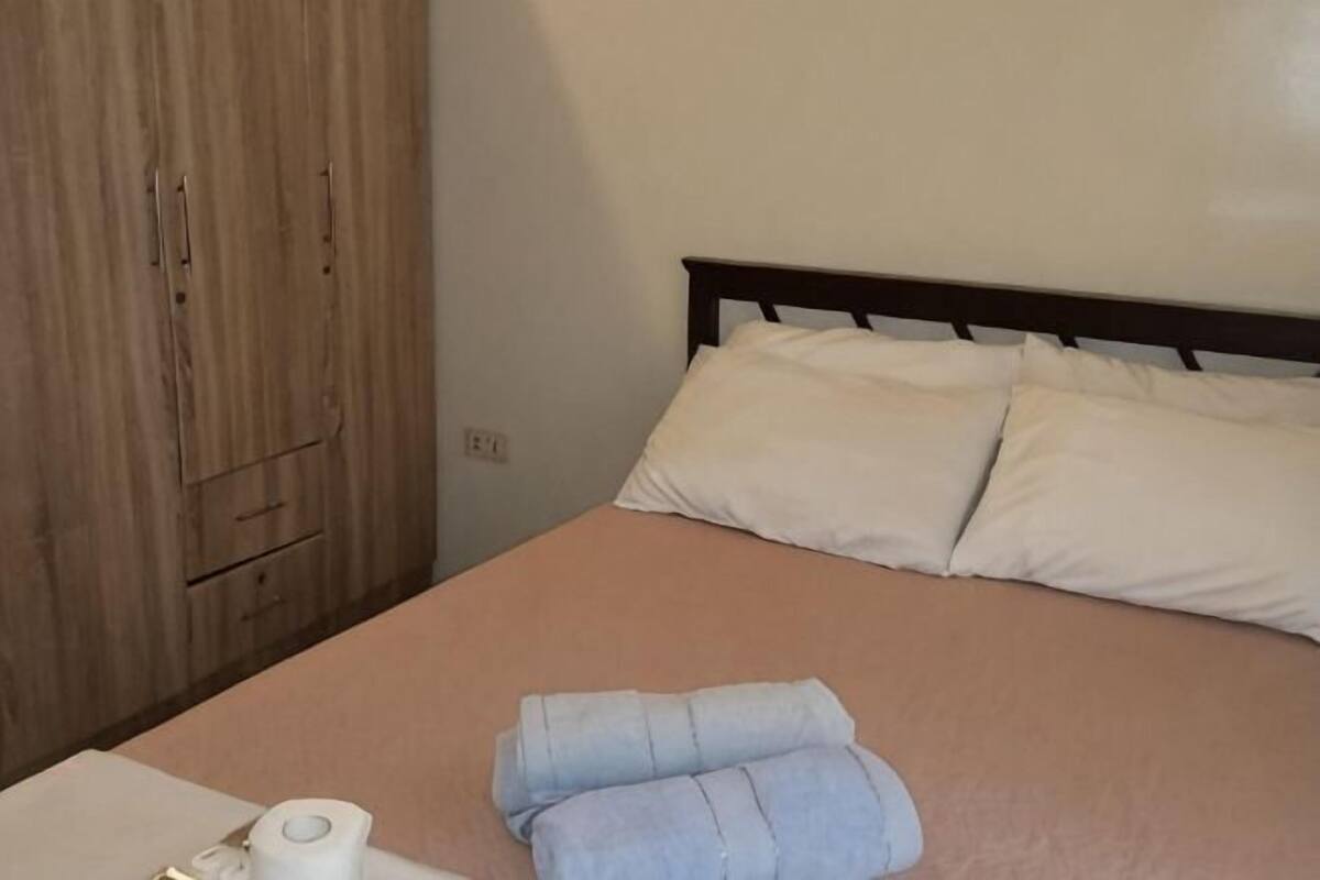 A bed with a wooden headboard, a beige blanket, and two rolled towels.