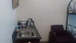 Eine kleine Küchenzeile mit Spüle, Wasserkocher, Kaffeemaschine und einigen Geschirrteilen.
