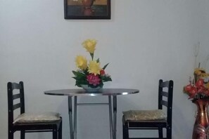 Un comedor con una mesa redonda, dos sillas y un florero con flores.