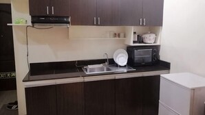 Eine Küche mit dunklen Schränken, einer Mikrowelle, einem Spülbecken und einem kleinen Kühlschrank.