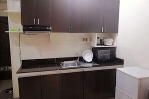 Una cocina con armarios oscuros, un microondas, un fregadero y un refrigerador pequeño.