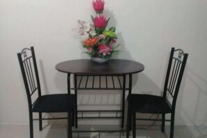 Una mesa redonda con dos sillas negras, un centro de mesa floral y una pared lisa de fondo.