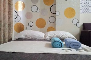 Un letto rifatto con cuscini e asciugamani arrotolati, una parete con motivi circolari e un decoro murale a fantasia.