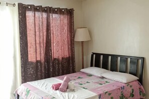 Ein Einzelbett mit Kopfteil, eine Nachttischlampe und ein Fenster mit Vorhängen.