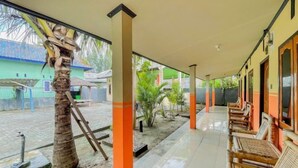 Un espacio al aire libre techado con una palmera, bancos de madera y piso de baldosas.